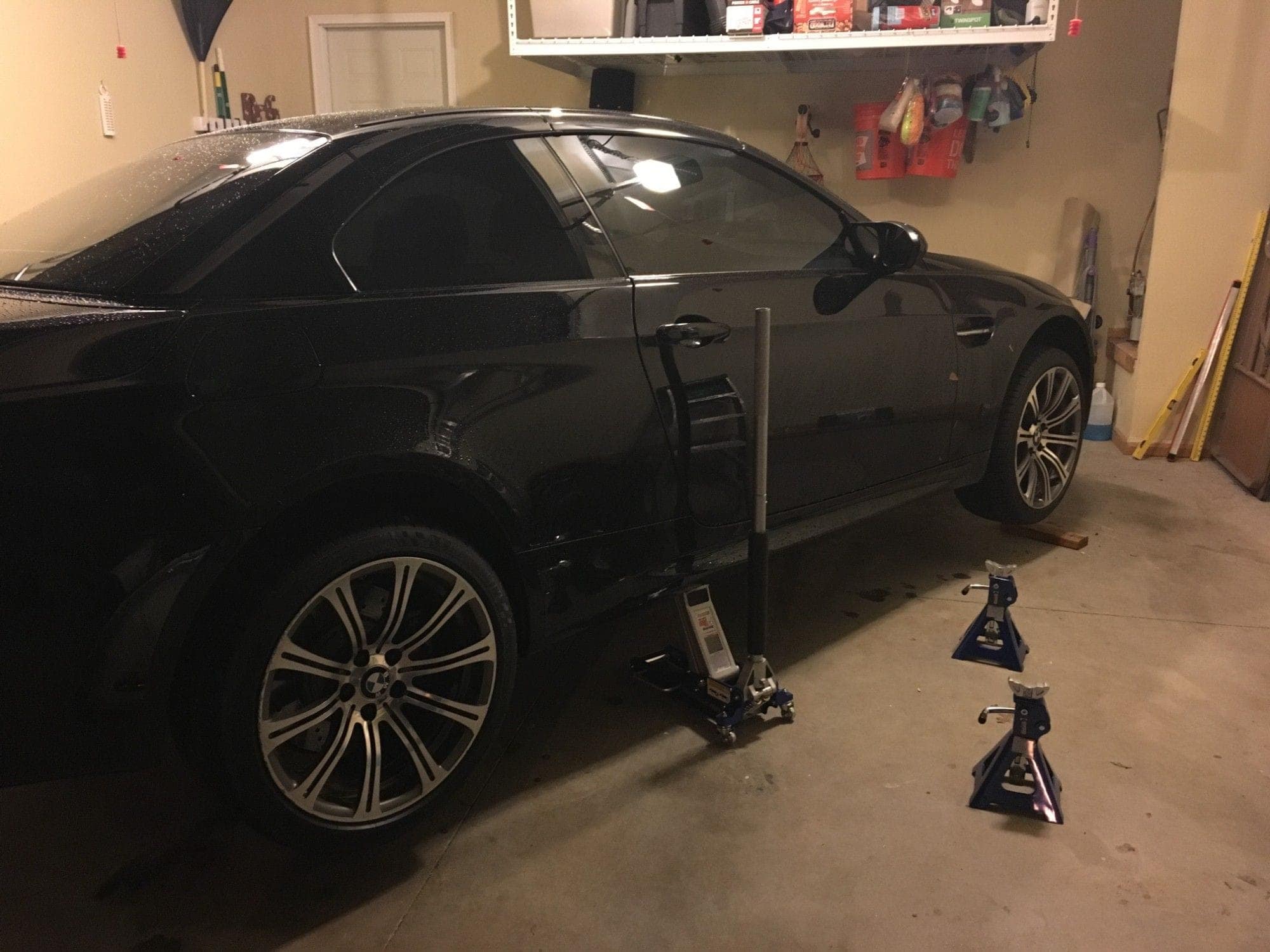 A black BMW M3 in a home garage with the wheels off, on jack stands
