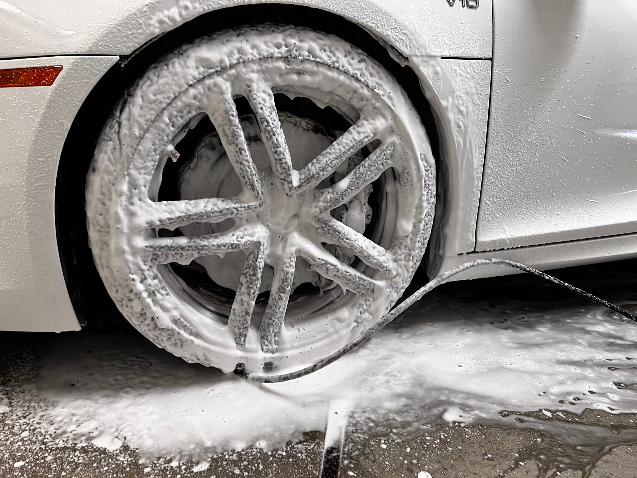 A wheel covered in foam during a wash, with the car behind it