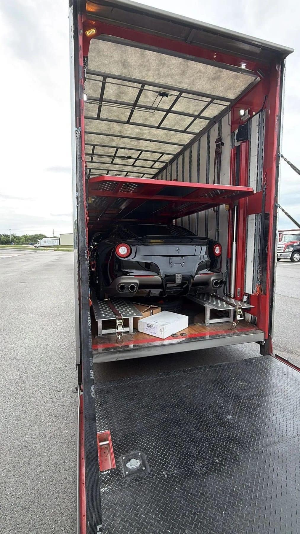 A Ferrari strapped on the upper deck of an enclosed car hauler, seen from the loading gate