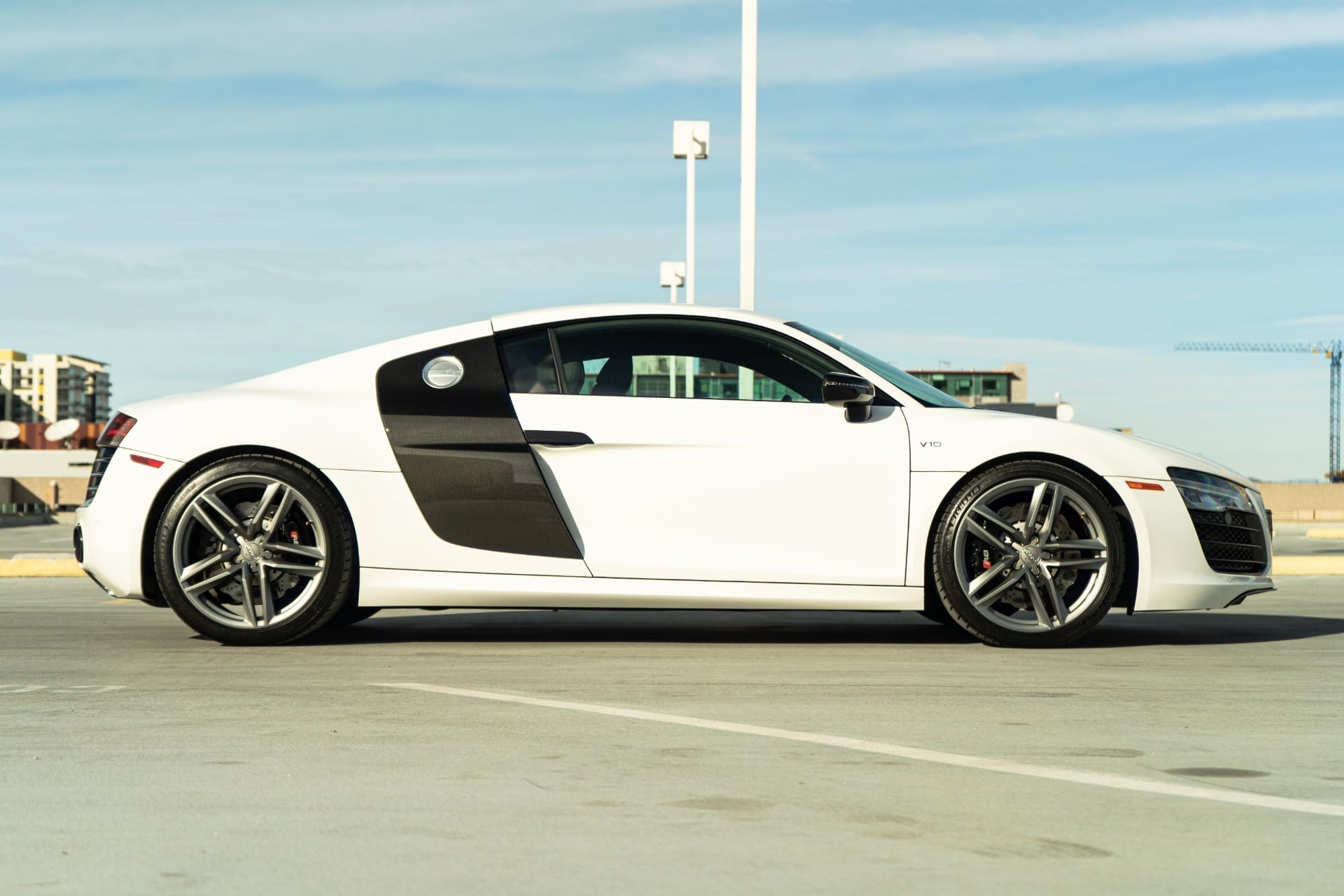 A white Audi R8 in profile on a parking deck under a blue sky