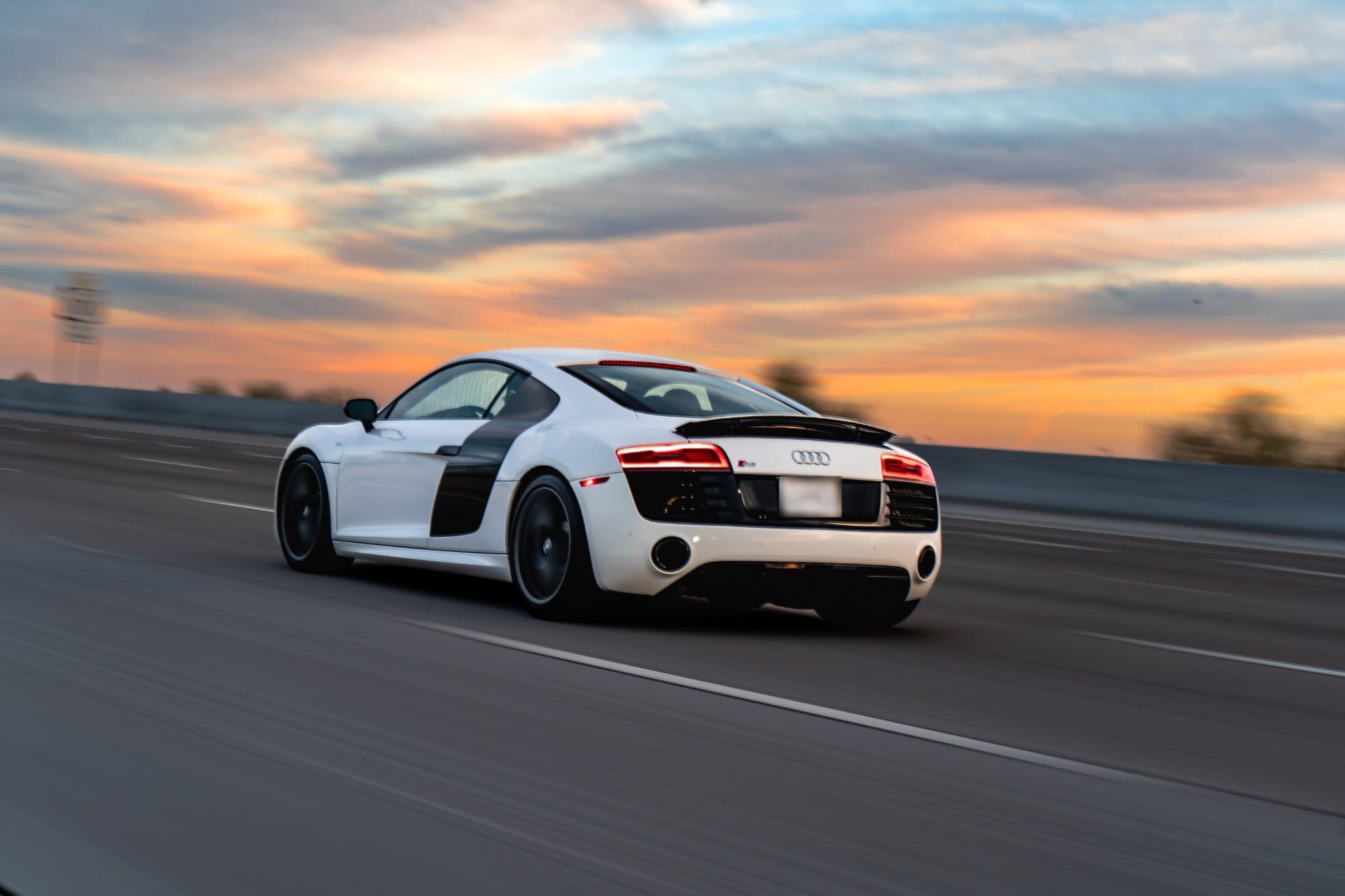 A white Audi R8 driving a road at sunset