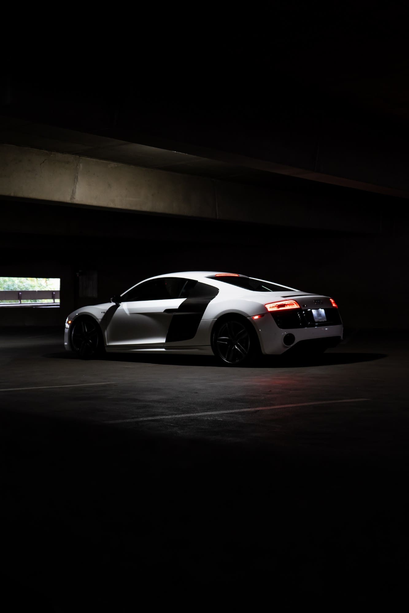 The rear three-quarter of a white Audi R8 lit in a dark parking structure