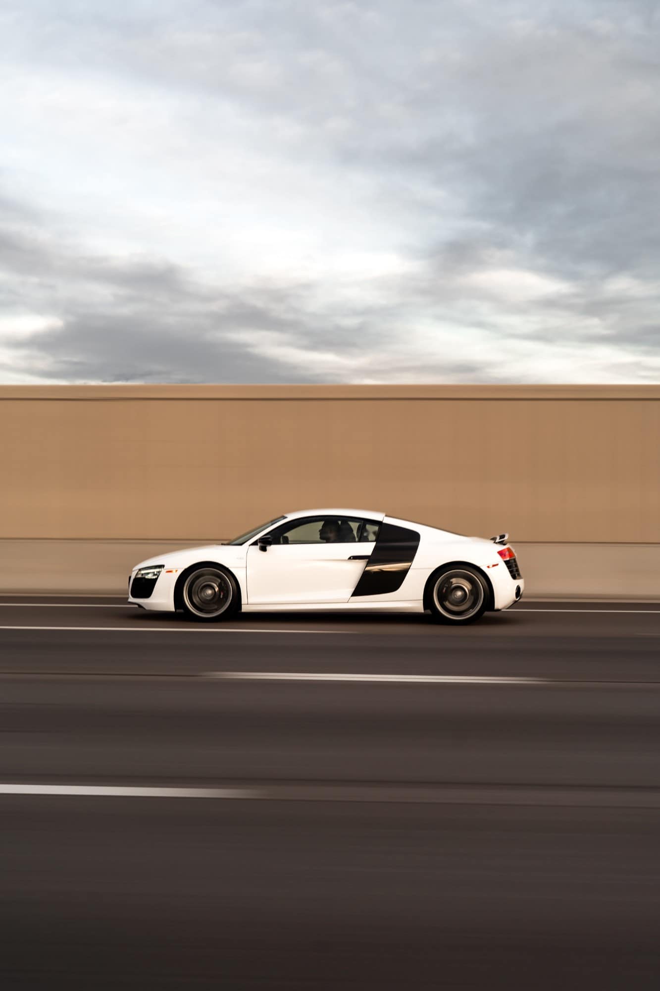 A white Audi R8 in a panning shot against a blurred wall