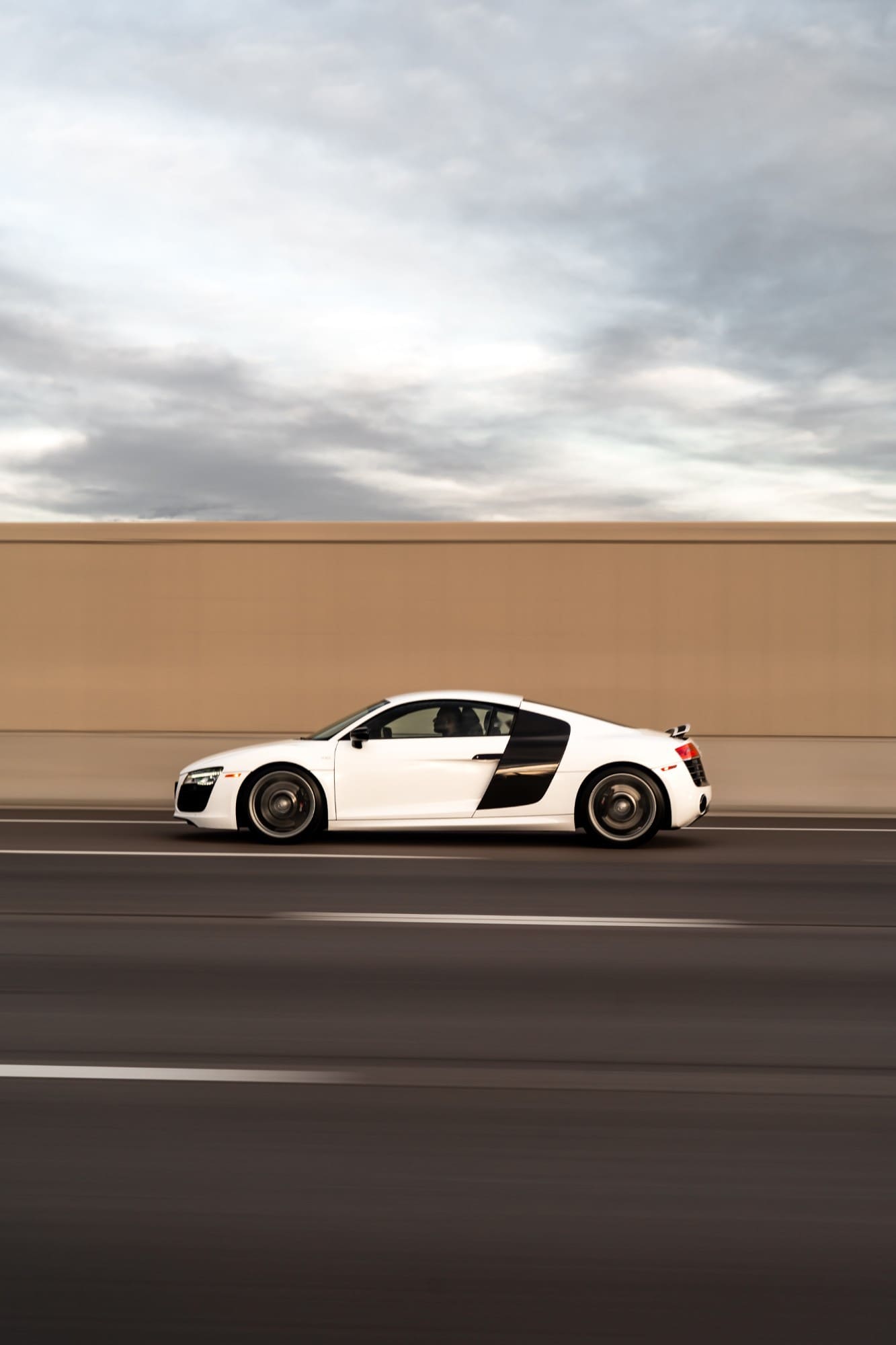 A white Audi R8 in a panning shot against a blurred wall