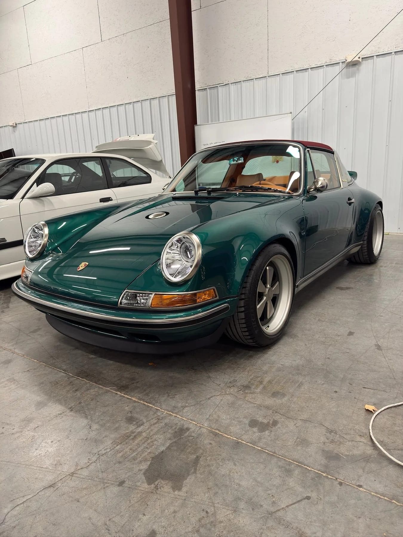 A green Singer-built Porsche 911 targa with a burgundy top in a metal-clad shop