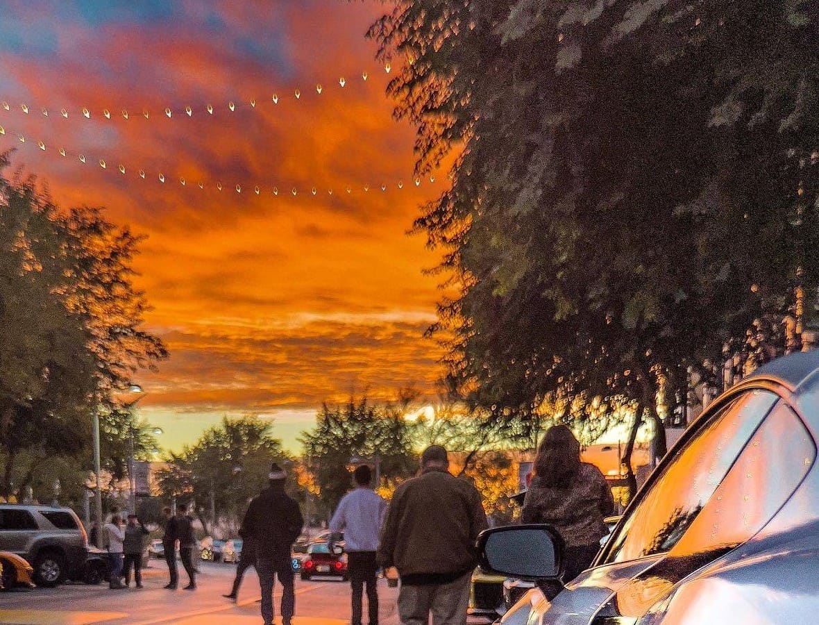 A street at dusk under string lights, guests walking between parked cars
