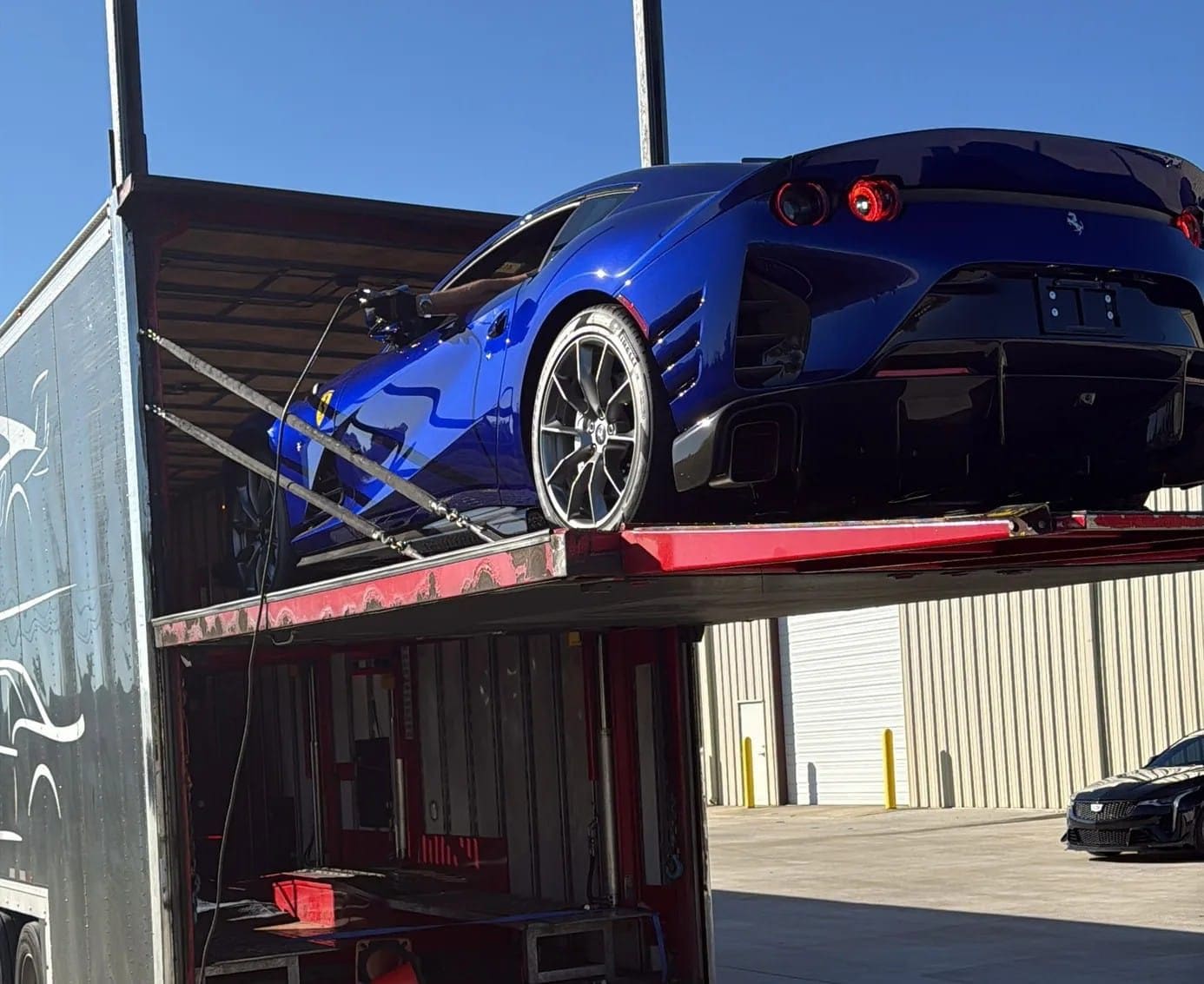 A blue Ferrari 812 Competizione on the top deck of a transporter, outdoors