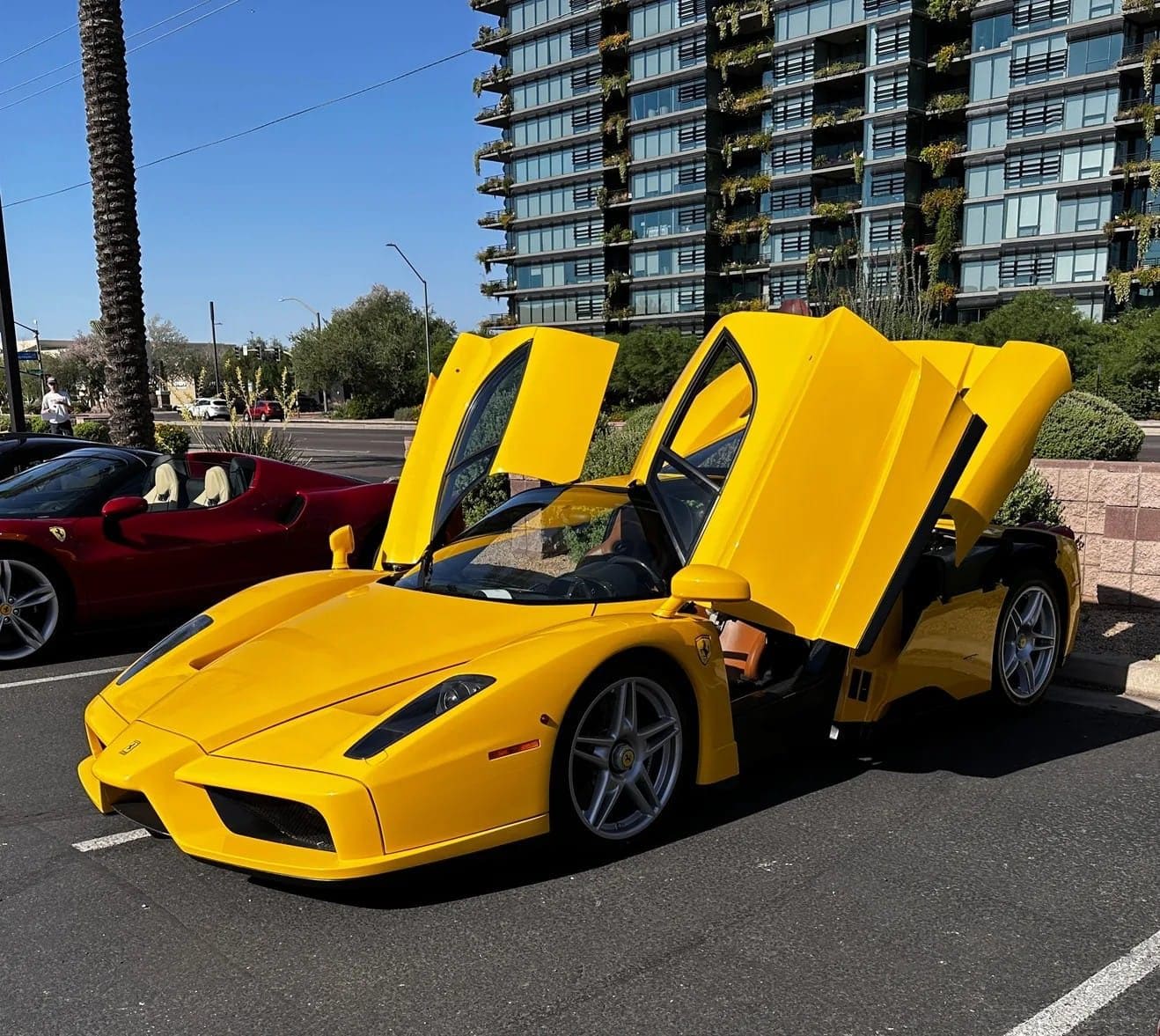 A yellow Ferrari Enzo with both doors up at Tires & Timepieces, with a condo tower behind it