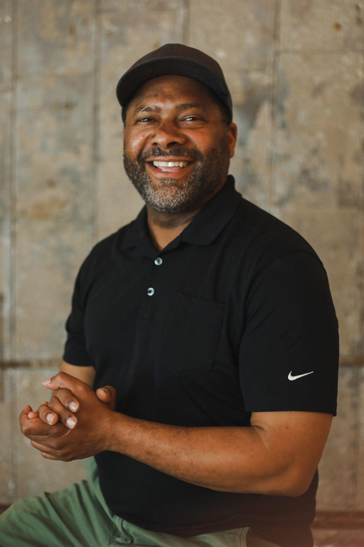 Gavin Brooks smiling at the camera, hands clasped, in a black polo and a cap